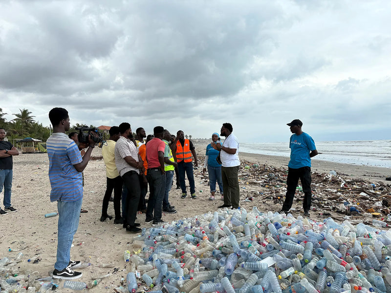 People standing beside a large pile of plastic bottles on a debris-covered beach