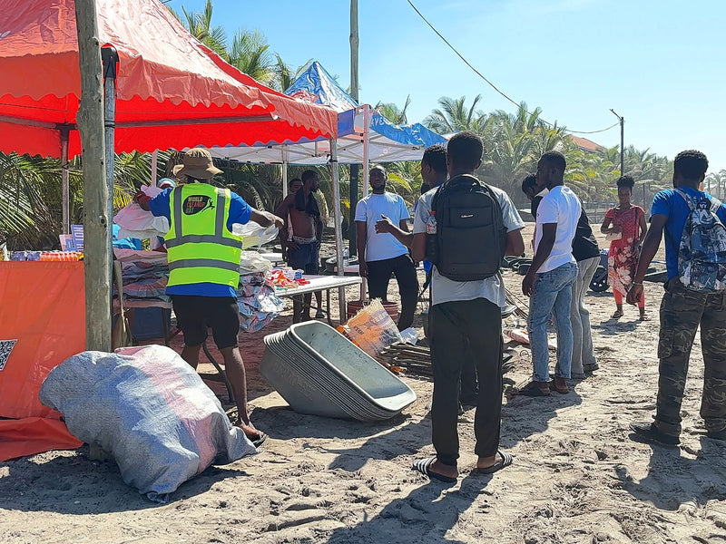 People gathered around red and blue tents with basins and sacks on the sand