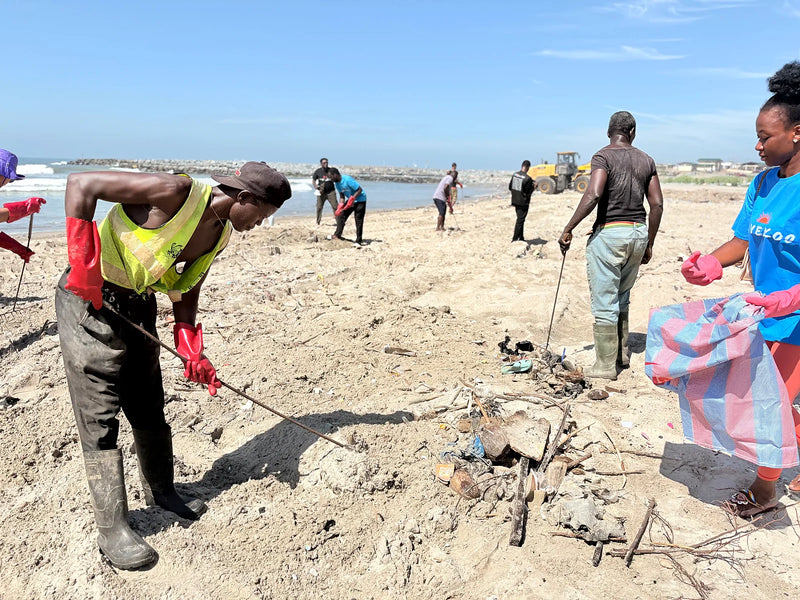Two people collecting debris; one holds a striped bag while another works the sand