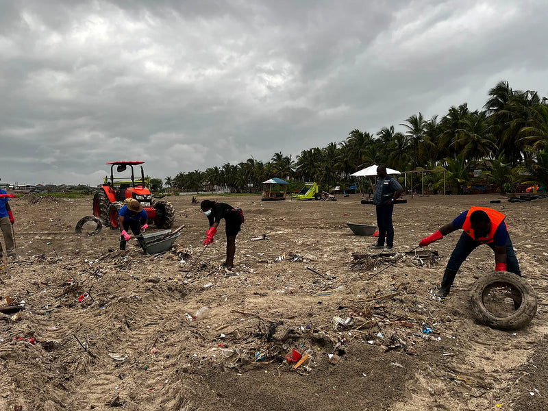 People collecting debris on a littered sandy field beside a tractor