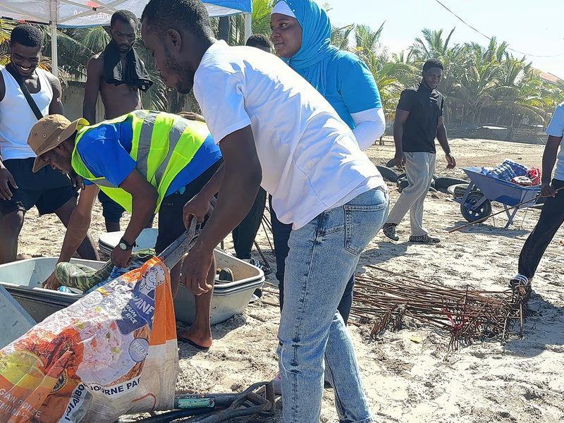 People sorting waste into sacks and tubs beside a wheelbarrow on sand