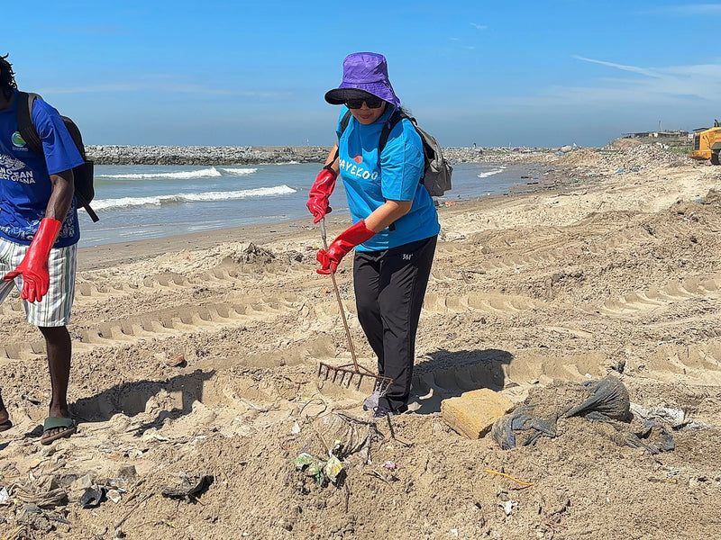 Person in red gloves raking debris on a sandy beach