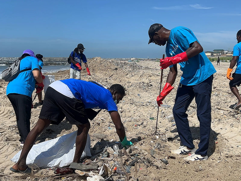 People in blue shirts raking and picking plastic waste into white bags