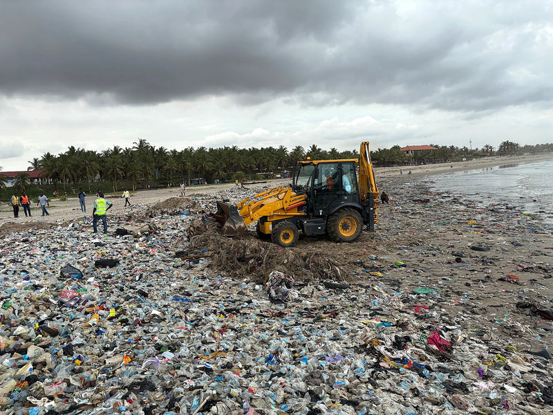 Yellow machine pushing through a wide field of plastic waste on a beach
