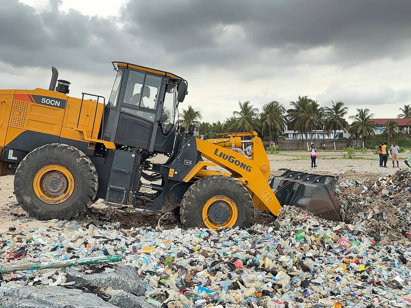 Yellow loader pushing its bucket into a dense pile of plastic waste
