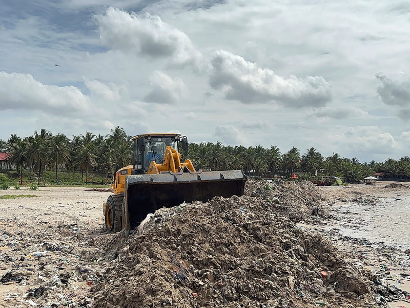 Yellow loader pushing a tall mound of mixed debris on a sandy beach