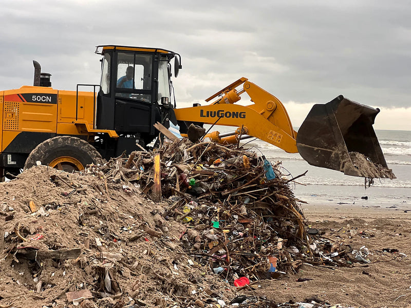 Yellow loader working a pile of plastic bottles and driftwood on a beach
