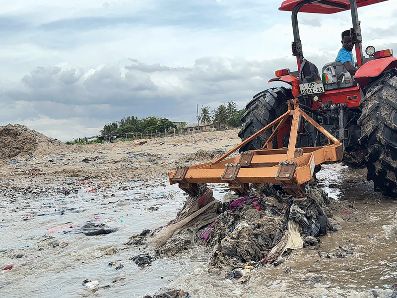 Red tractor dragging a rake through wet, tangled waste