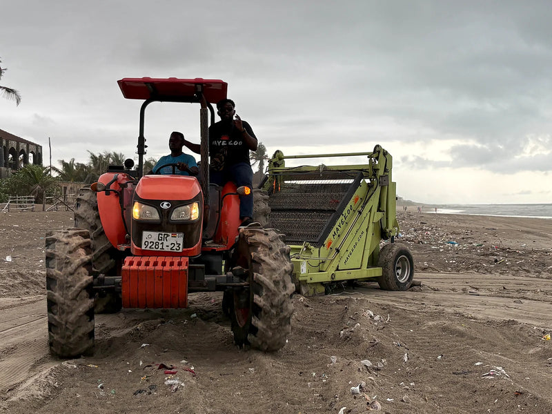 Red tractor towing a green beach-cleaning machine across sand