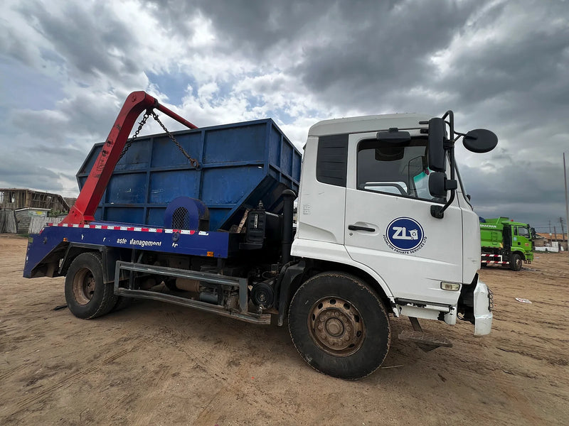 Waste-collection truck carrying a blue skip container on sandy ground