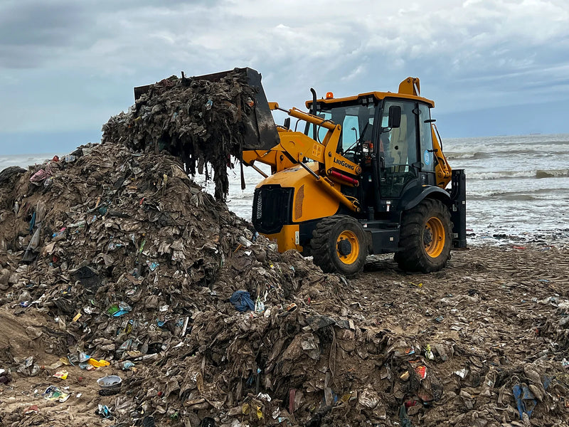 Yellow loader adding wet debris to a large waste pile on a beach