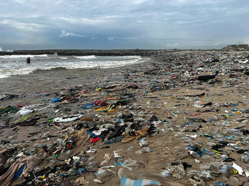 Shoreline densely covered in plastic bags and discarded fabric near the water