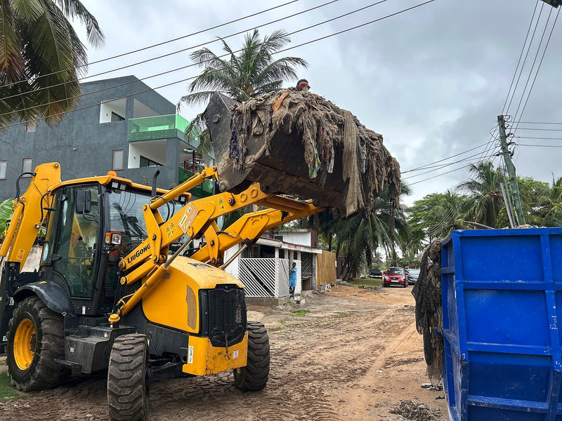 Yellow loader lifting a bucket of tangled waste toward a blue skip