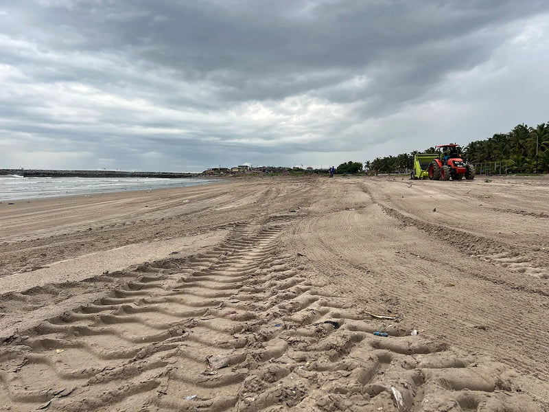 Red tractor pulling a green beach-cleaning attachment across sand