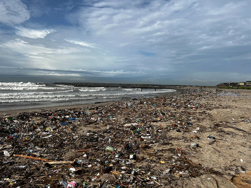Wide shoreline covered in a dense layer of plastic and mixed waste