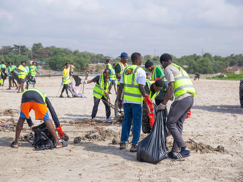 People in yellow vests placing debris into a black collection bag