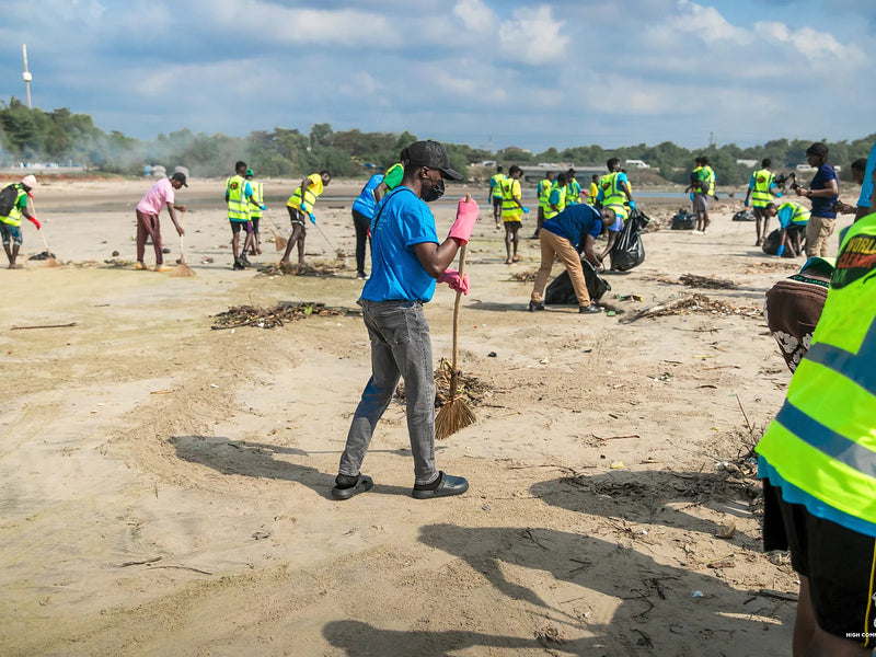 Person sweeping sand with a twig broom while others collect waste nearby