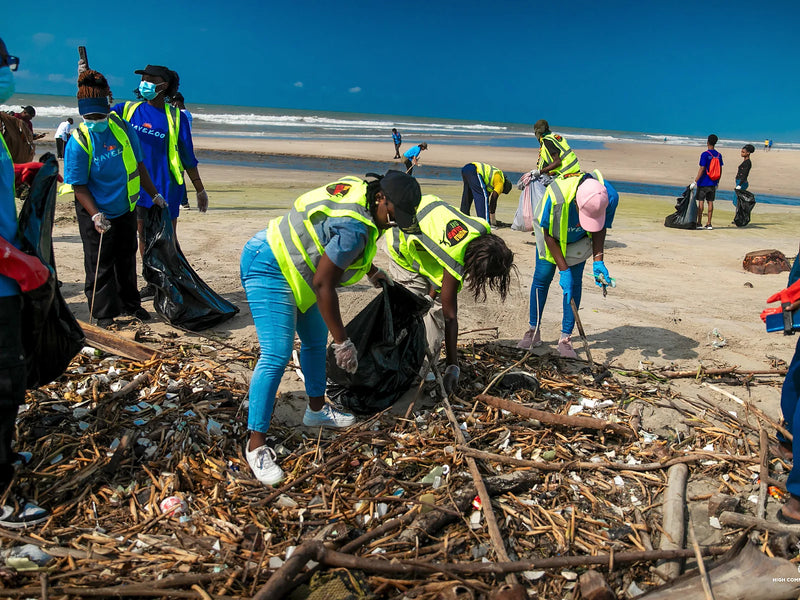 People in yellow safety vests filling black bags from a debris pile on a beach