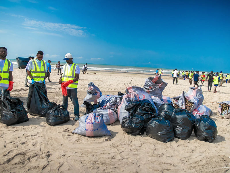 Filled black and grey collection bags on sand with people in safety vests nearby
