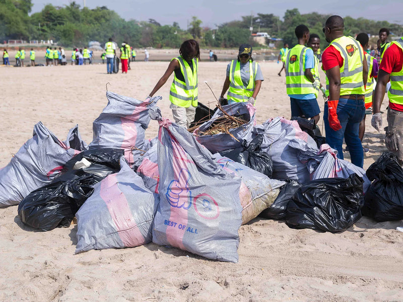 Close view of filled woven sacks and black bags stacked on sand