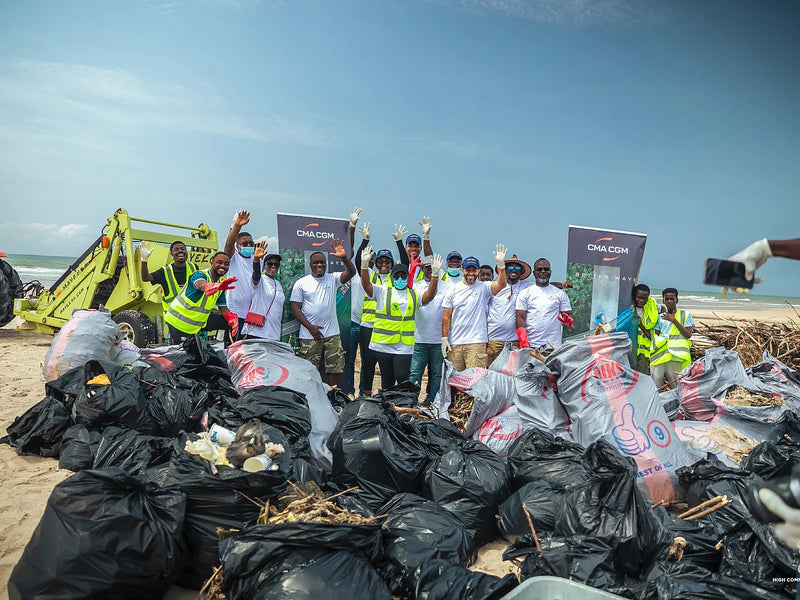 Group standing behind a large pile of filled trash bags on a beach