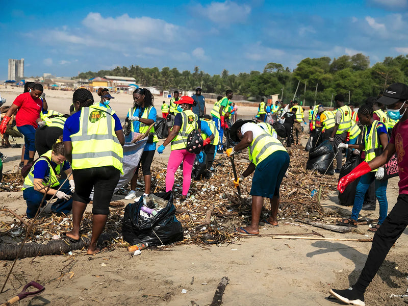 Many people in yellow vests clearing a long line of driftwood and litter