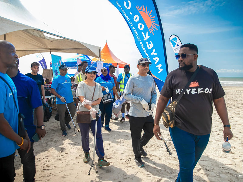 People walking on sand with litter grabbers beside a tall blue flag and tents