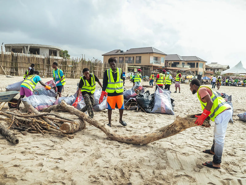 People in yellow vests lifting large pieces of driftwood beside filled bags