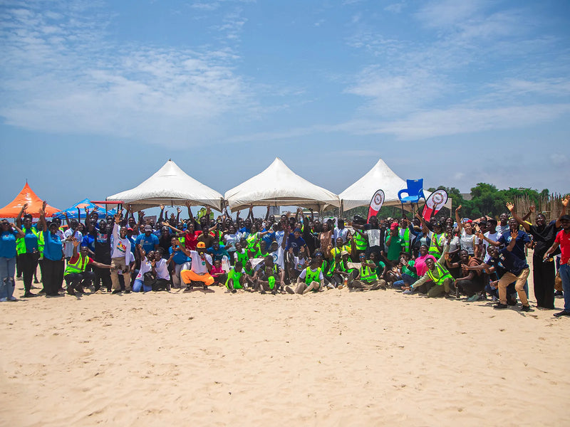Large crowd in safety vests posing on a sandy beach in front of white tents