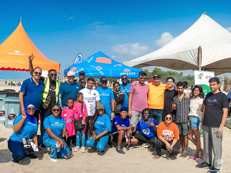 Group posing on sand in front of tents and collection bins