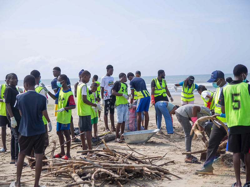 Young people in yellow vests gathering driftwood and bags on a beach