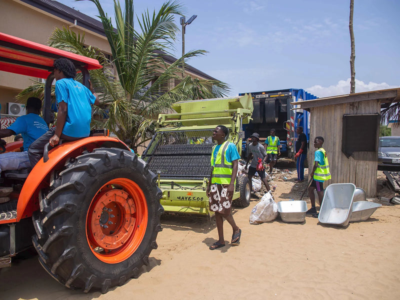 Tractor, mayekoo beach rake, bins, and a waste truck on a sandy staging area