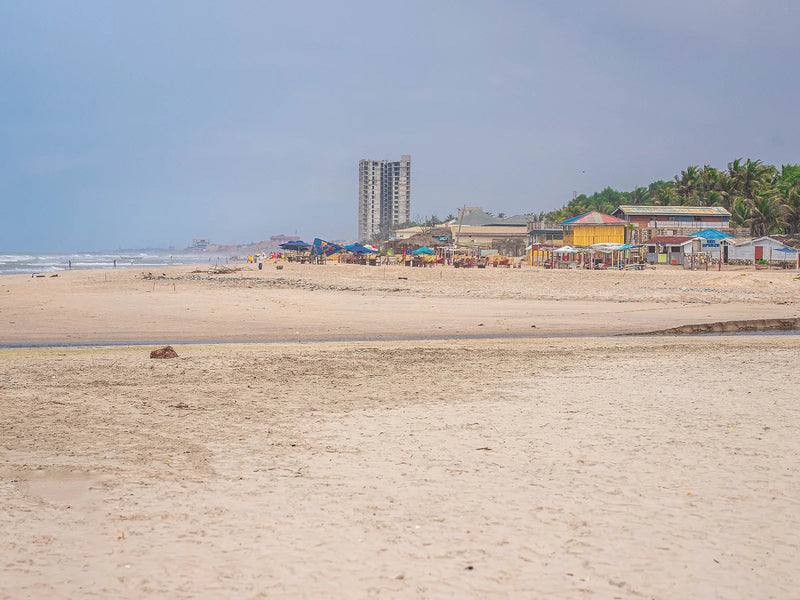 Wide sandy beach with umbrellas, low buildings, and ocean under an overcast sky